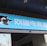A building entrance features a vibrant blue sign with white Chinese characters and a stylized orca logo in black and white. The overall appearance suggests an establishment focused on eSports or digital activities.
